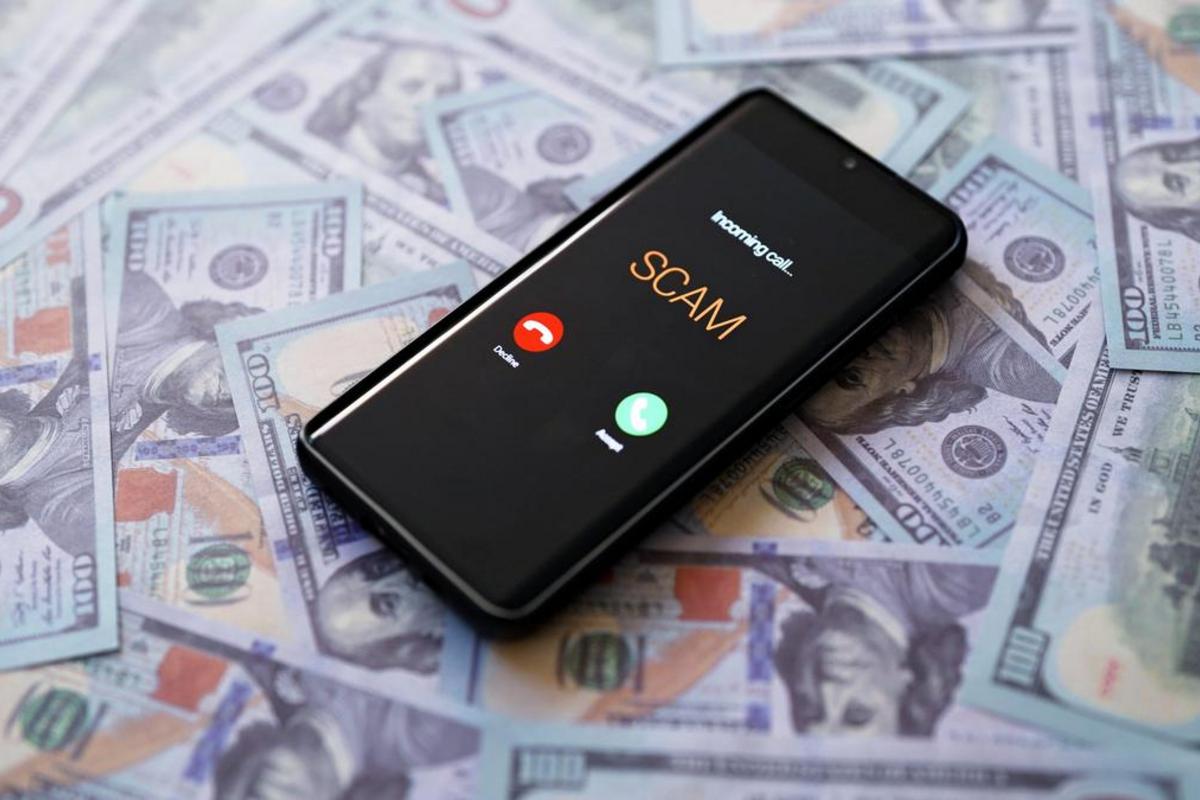 Smartphone displaying an incoming call labeled SCAM on top of a pile of hundred-dollar bills.